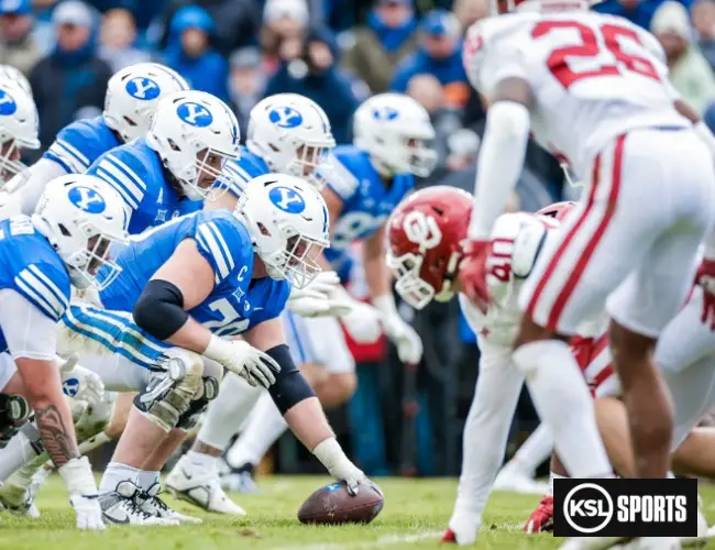 A photo of BYU and OU football teams during their football match at the Lavell Edwards Stadium. BYU's team is in blue while Oklahoma University is in red