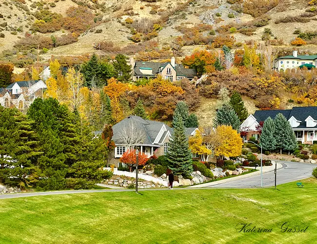 Photo of a vibrant community in Provo Utah with vast mountain ranges in the background and surrounded by autumn trees. Photo by Katerina Gasset and Tristan Gasset, licensed Realtors in Provo and Orem Utah