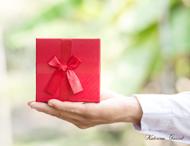 Image showing a gift inside a box wrapped in red ribbon and gift wrapper. Photo by Katerina Gasset of the Gasset Group Real Estate Team in Utah